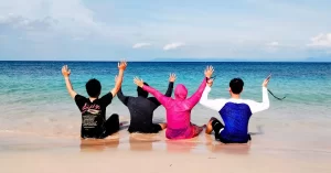 Empat peserta Tour Lombok duduk di tepi pantai menikmati pemandangan laut biru