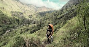 Pendaki menuruni jalur Torean Gunung Rinjani dengan latar lembah hijau nan indah.