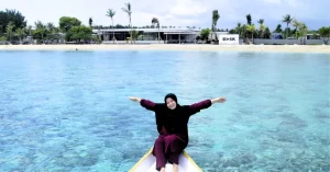 Seorang wisatawan wanita duduk santai di ujung perahu dengan latar laut jernih dan pantai Gili Trawangan dalam program Tour Gili Trawangan
