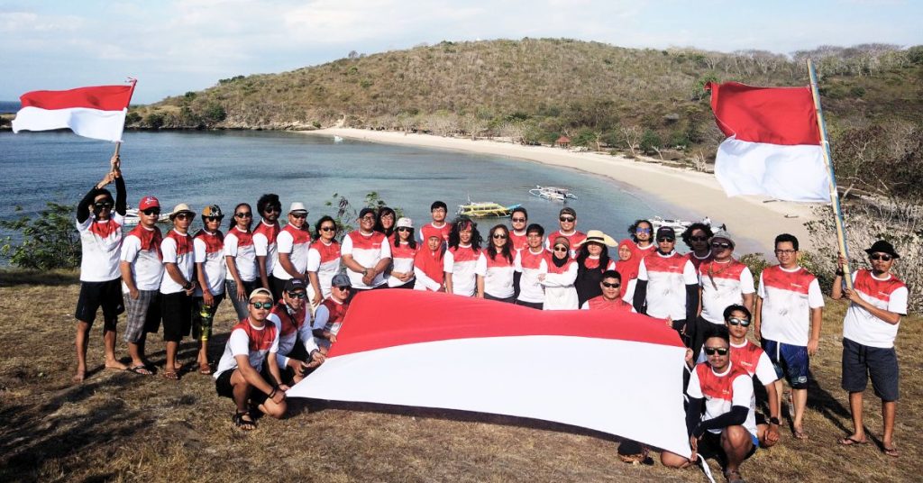 Peserta outing kantor mengikuti paket tour group Lombok dengan latar pantai eksotis dan bendera merah putih
