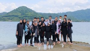 Grup wisatawan berpose bersama di pantai dengan latar bukit hijau di Lombok