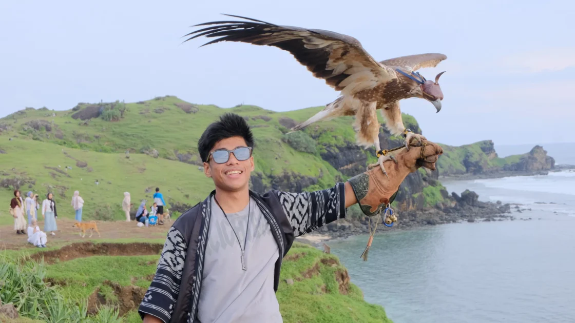 Wisatawan berfoto dengan burung elang di Bukit Merese sambil menikmati pemandangan menjelang sunset saat mengikuti Paket Wisata Lombok 5 Hari 4 Malam Opsi C.